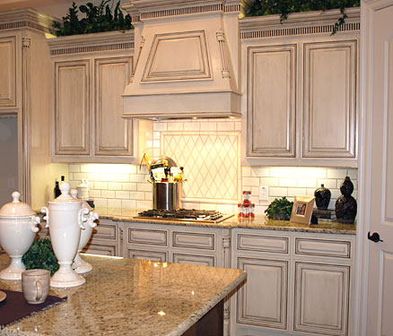 Glazed white kitchen cabinets in combination with countertops and backsplashes of light natural stone
