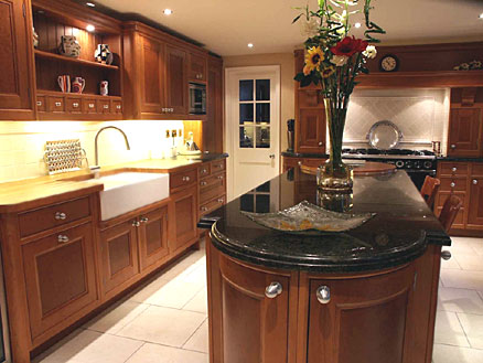 Traditional kitchen design - brown wood cabinets, apron front sink, black marble countertop, and light tile backsplashes and floor