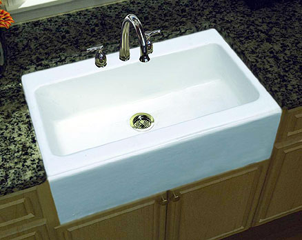A farmhouse apron front single bowl white cast iron kitchen sink in combination with granite counters and wood cabinets