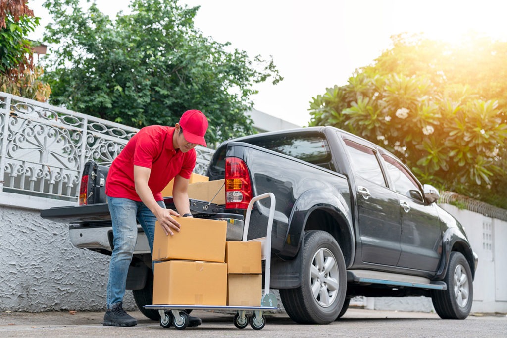 Delivery men in red uniform unloading cardboard boxes from pickup truck