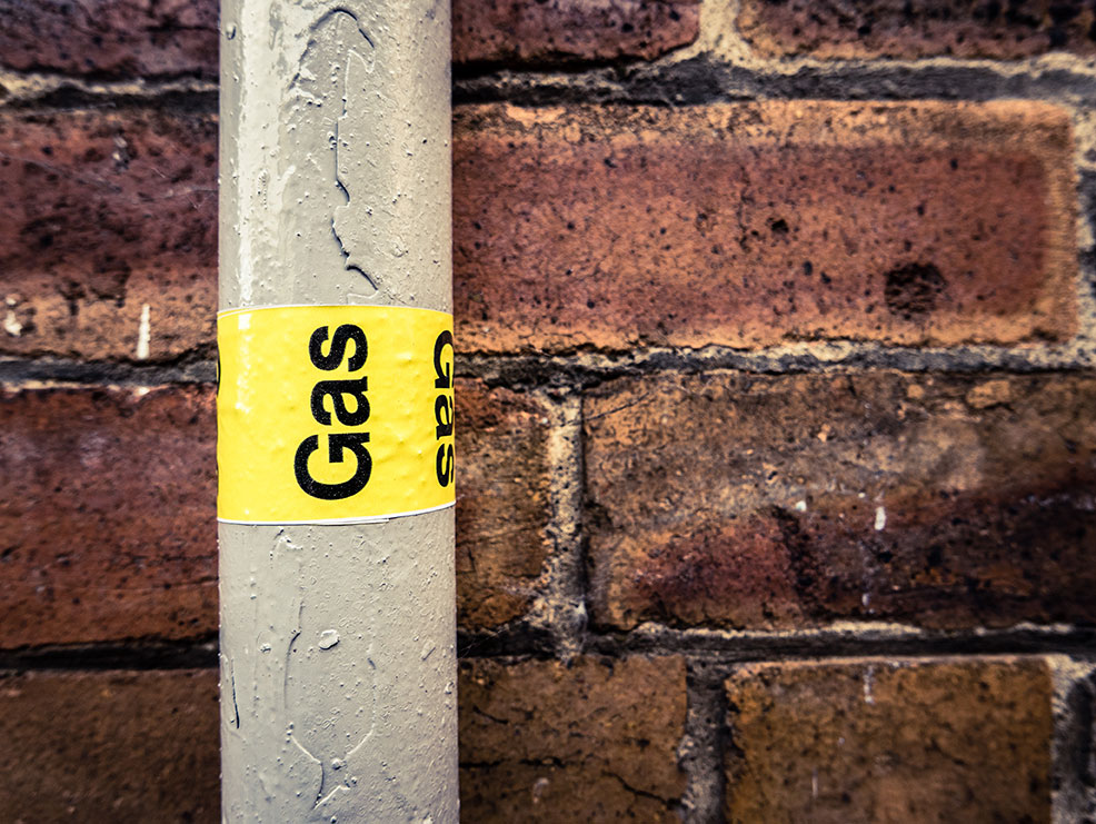 Detail of a residential gas pipe against a red brick wall.