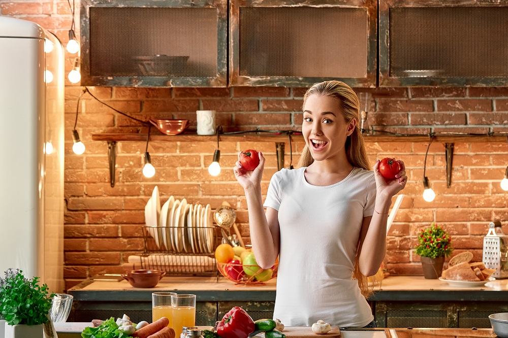 Portrait of blonde girl wearing white T-shirt, holding tomatoes, looking at the camera and smiling