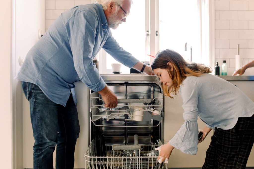 Two persons putting dirty dishes in a dishwasher.