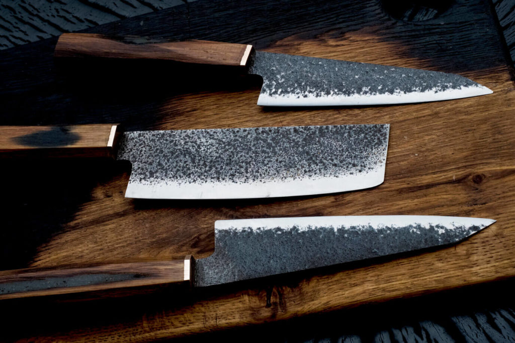 Damascus steel kitchen knives with brown wooden handles. The set includes two chef knives and a cleaver.