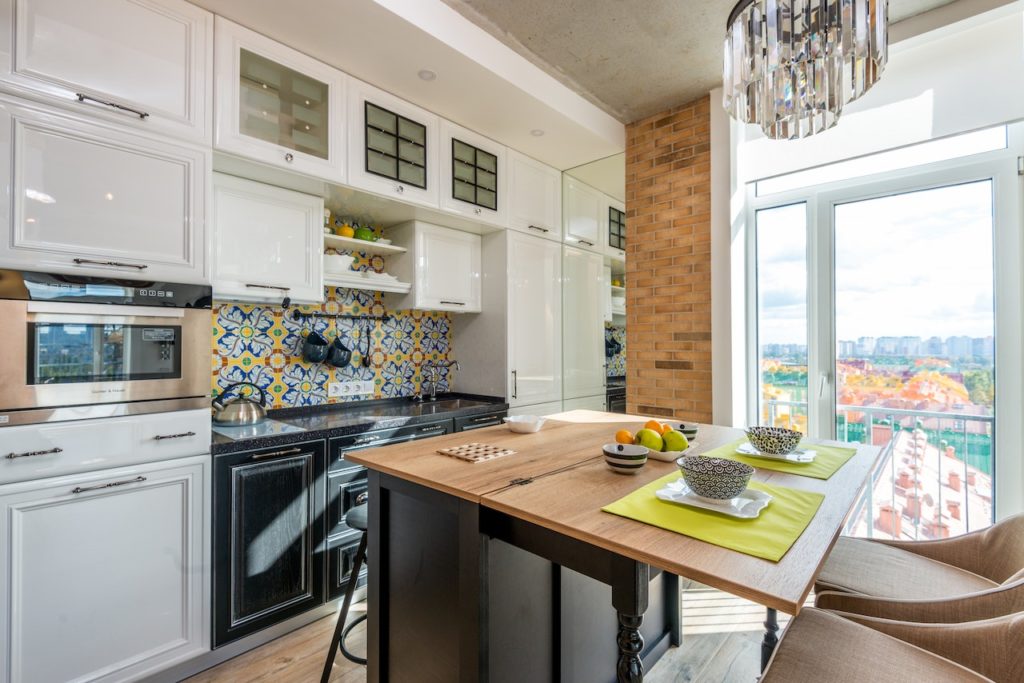 A kitchen with white cabinets, black counters and a mosaic backsplash. There is a kitchen island with a wooden countertop in the center of the room as well.