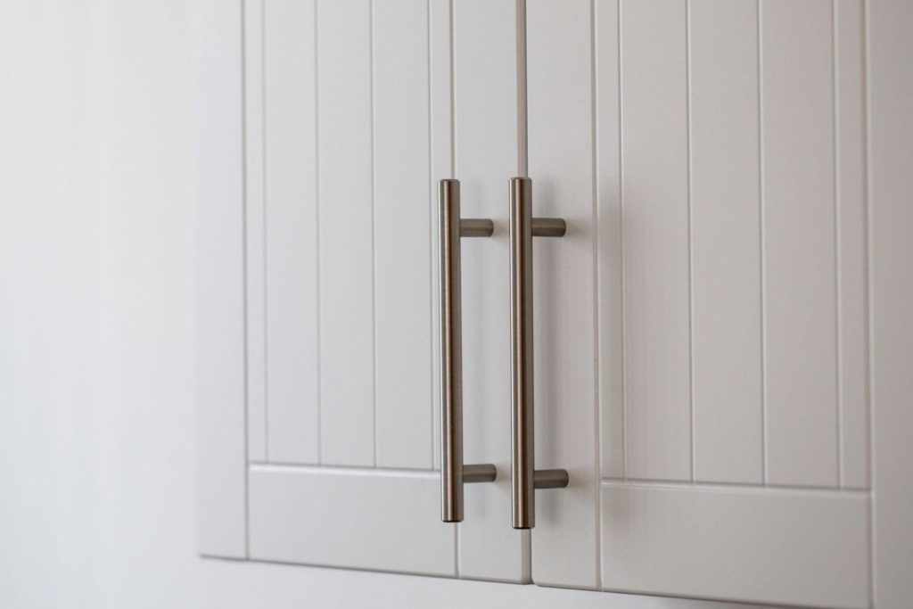 Long vertical stylish metal pulls attached to white kitchen cabinets.