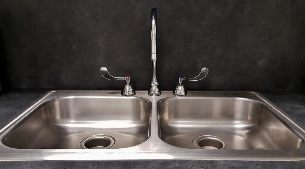 A double basin stainless steel kitchen sink with stainless steel kitchen faucet.