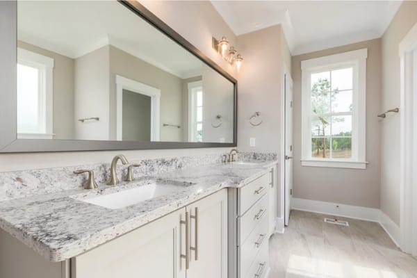 Concrete countertops with white cabinets. There is a big rectangular mirror above the two faucets.