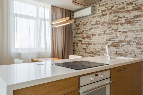 A kitchen island with white concrete countertops and wood cabinets. There is an oven, a cooktop and a sink with faucet.