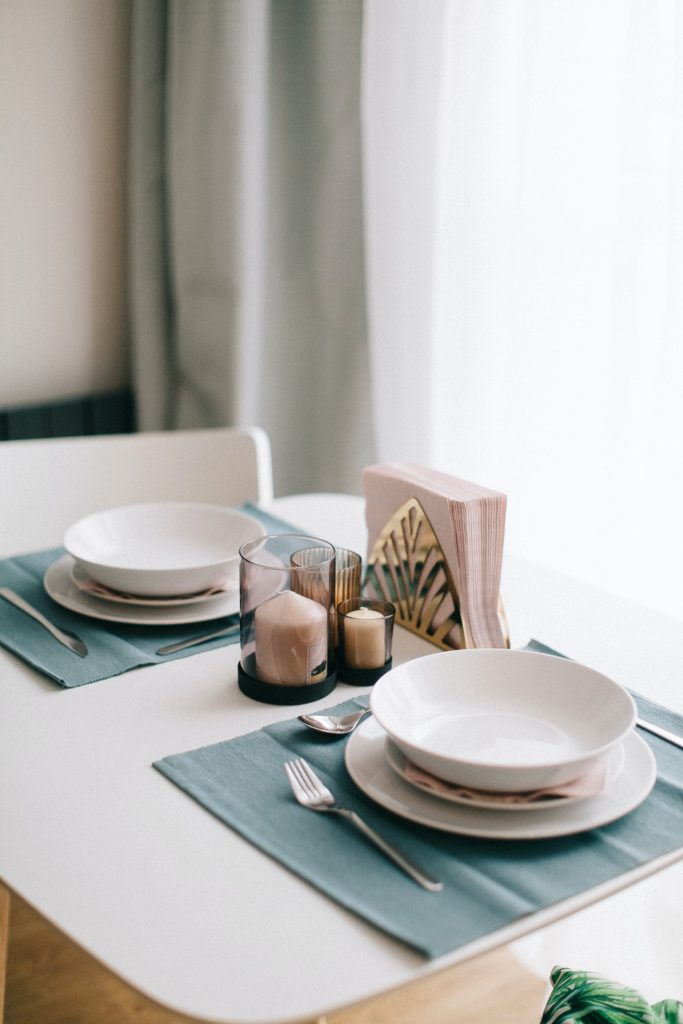 A beautifully organized dinnerware set including plates, linens, napkins, utensils and candleholders.