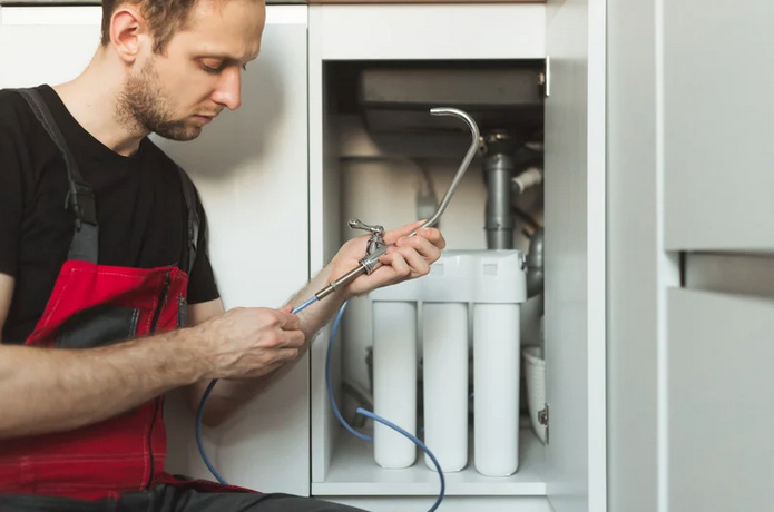 A man installing a water filtration system beneath a kitchen sink.